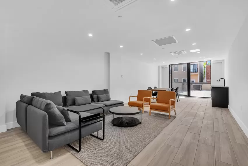 Project 3610, a modern living room by Total Building Solutions, featuring a large grey sofa, a round black coffee table, and two orange chairs.